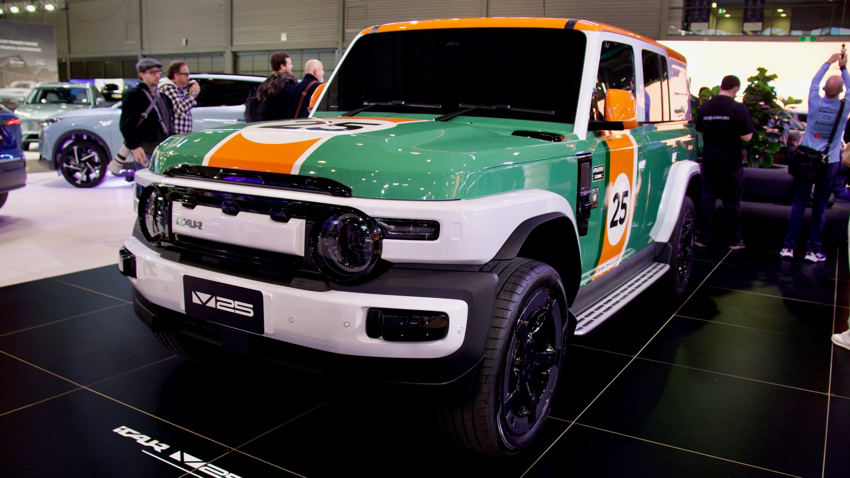 Front three-quarter view of a green, orange, and white pickup with racing livery, number 25, on display at an indoor car show