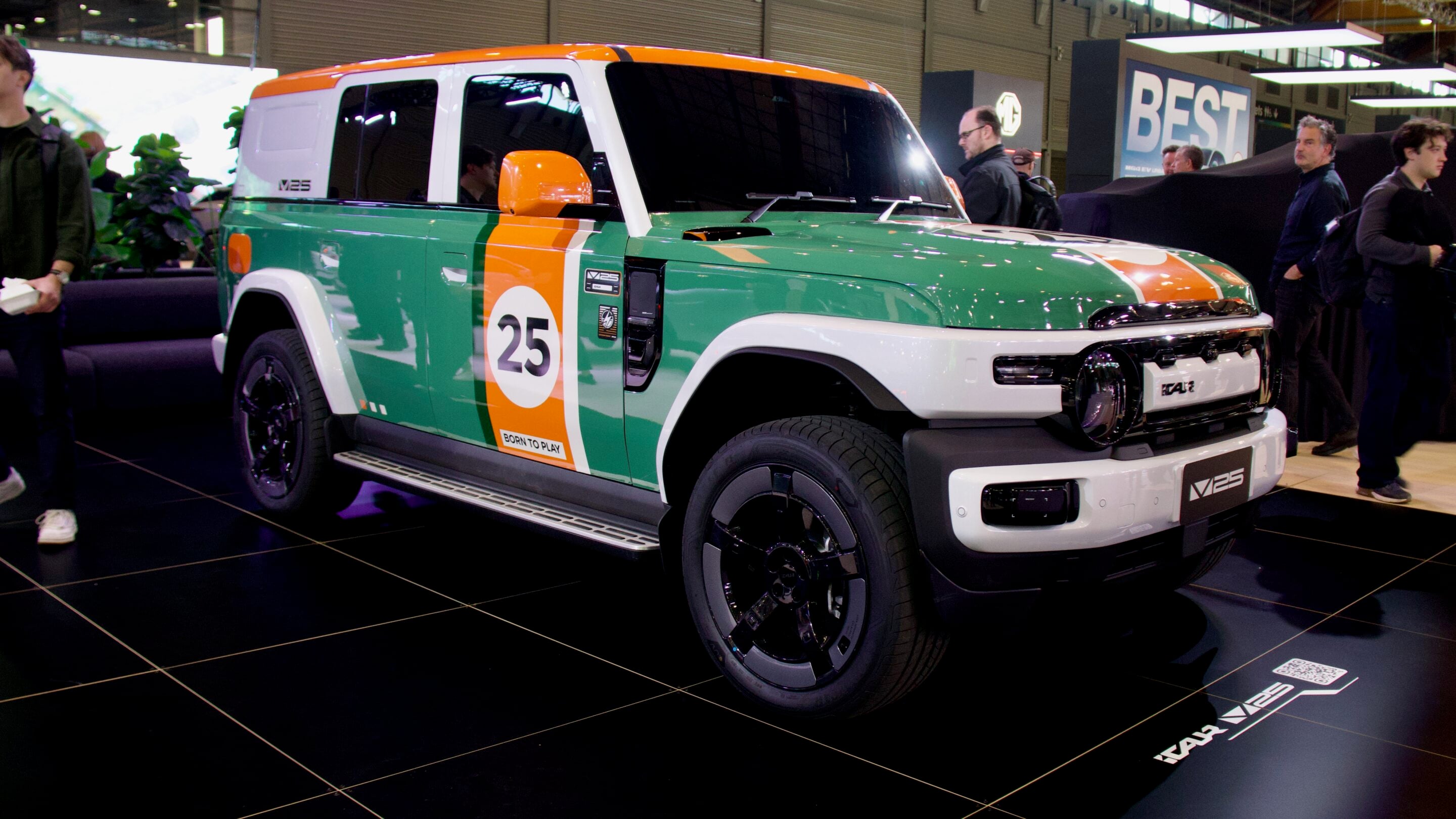 Green and orange racing-style SUV on display at an auto show, number 25 on the door and 'Born to Play' label visible, surrounded by attendees.