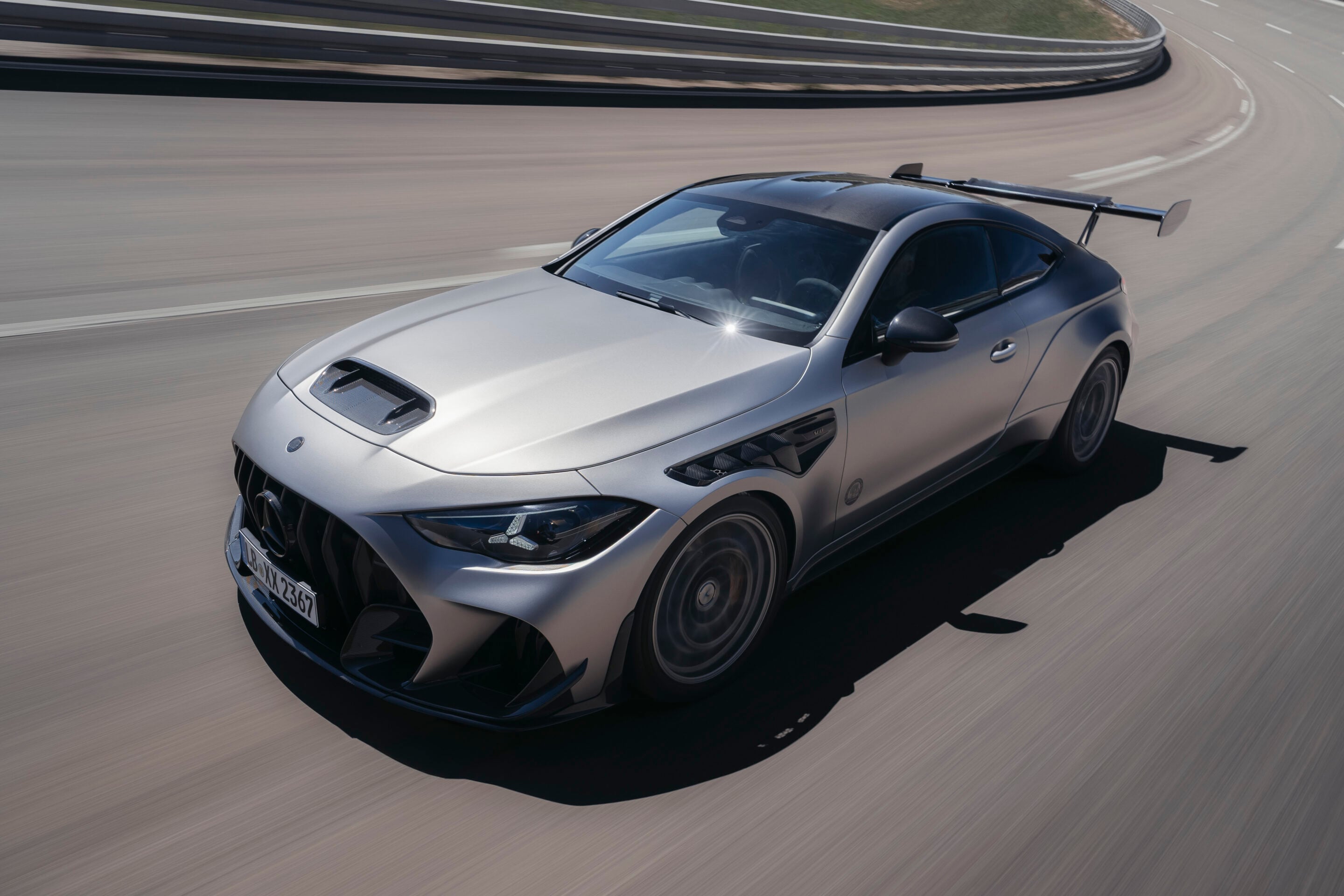 Silver high-performance car with a large rear wing speeds along a curved race track.