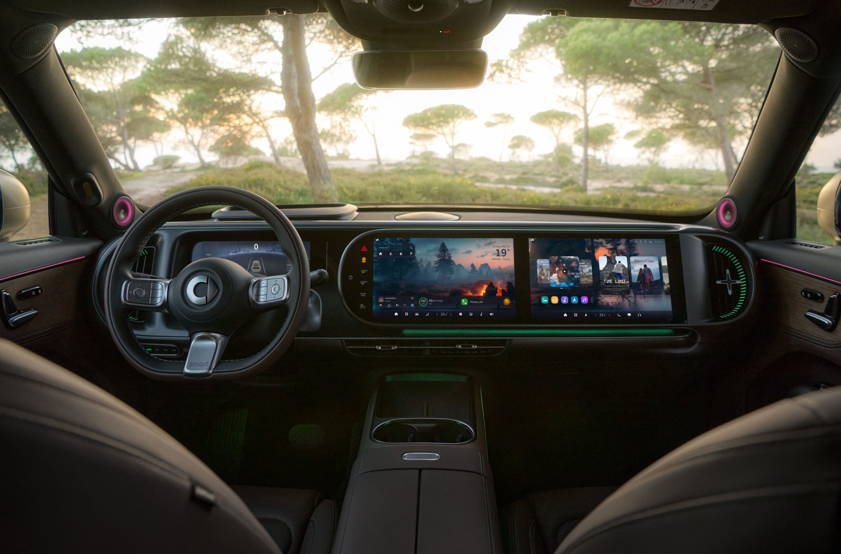 Interior of a modern car cockpit with large curved digital screens across the dashboard and a forest visible through the windshield.