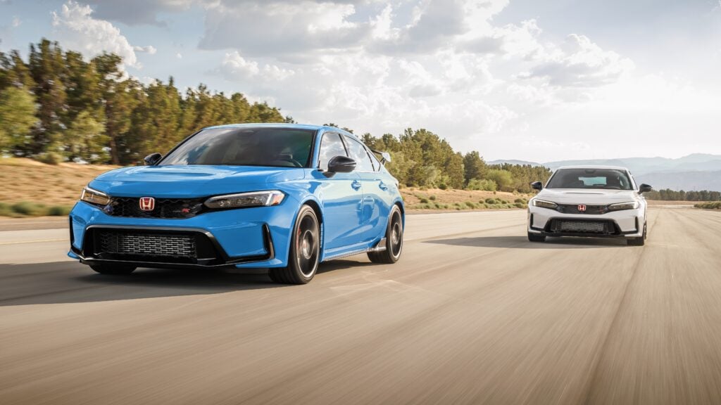 Blue Honda Civic Type R leads a white Honda Civic on a sunny open highway, desert landscape and distant mountains in view.