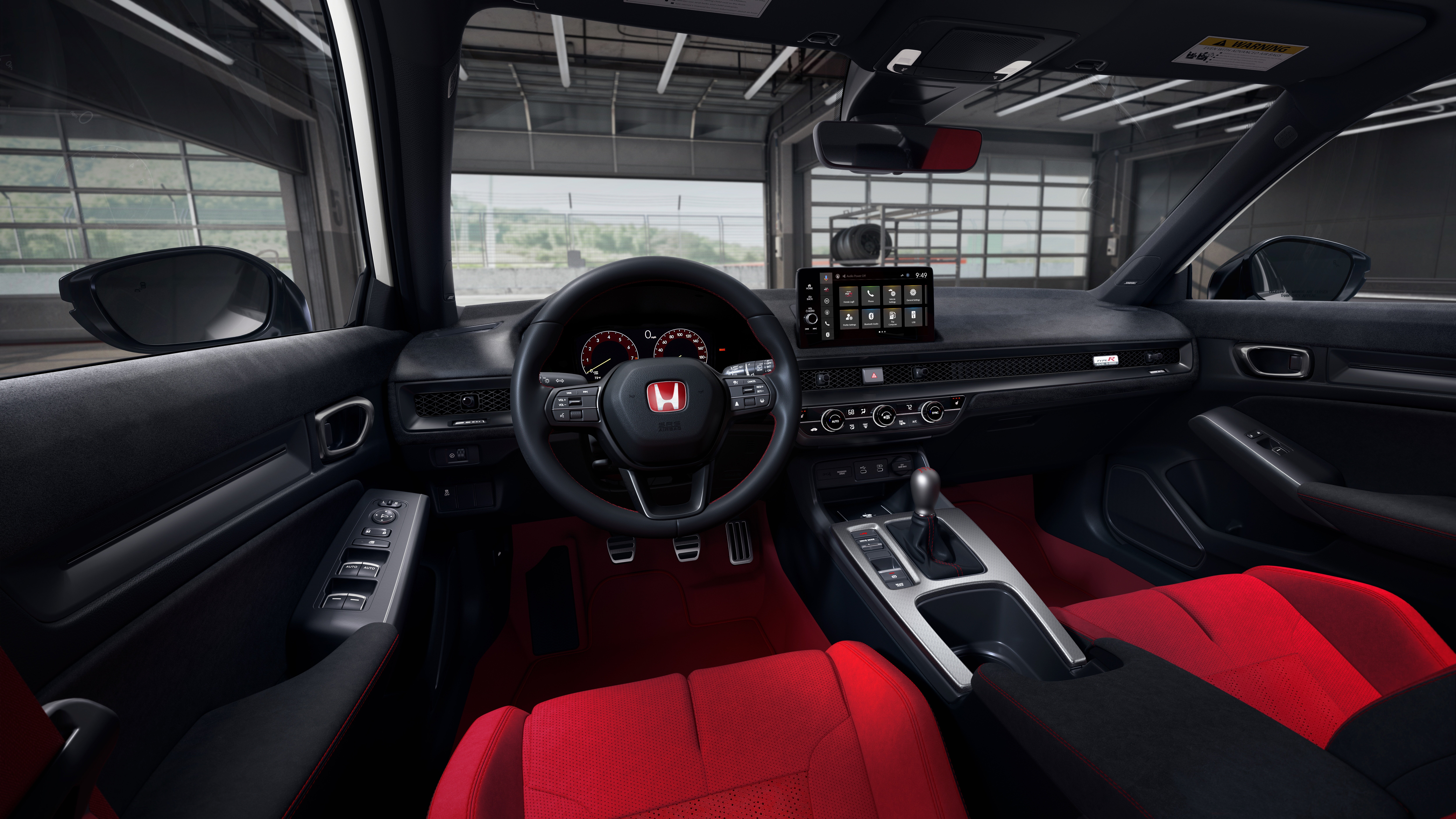 Car interior with a right-hand drive setup, red seats, and a large center infotainment screen on the dash behind the steering wheel.