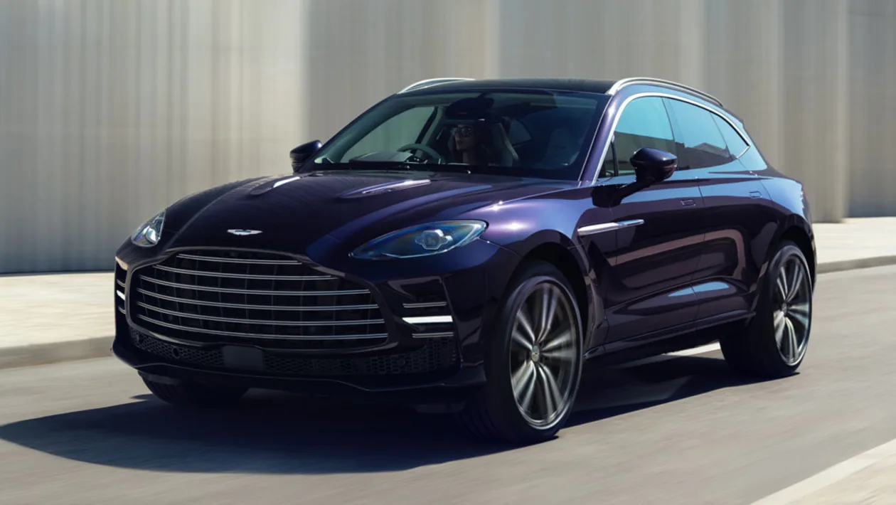 Front three-quarter view of a dark purple luxury SUV driving on a city street, featuring a large chrome grille and stylish alloy wheels.