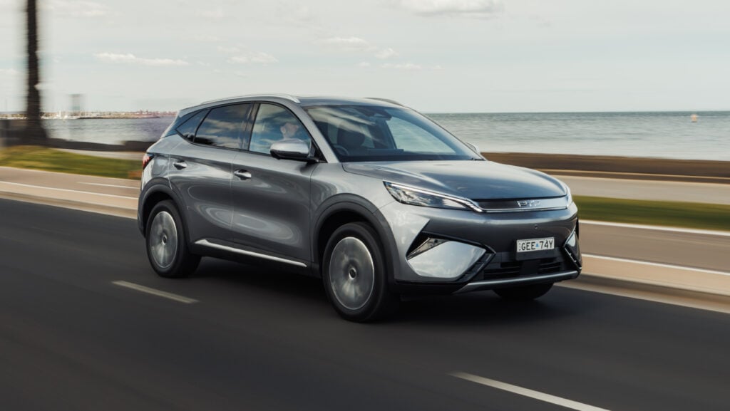 Silver SUV driving along a coastal highway with the sea and sky in the background, motion blur suggesting speed.