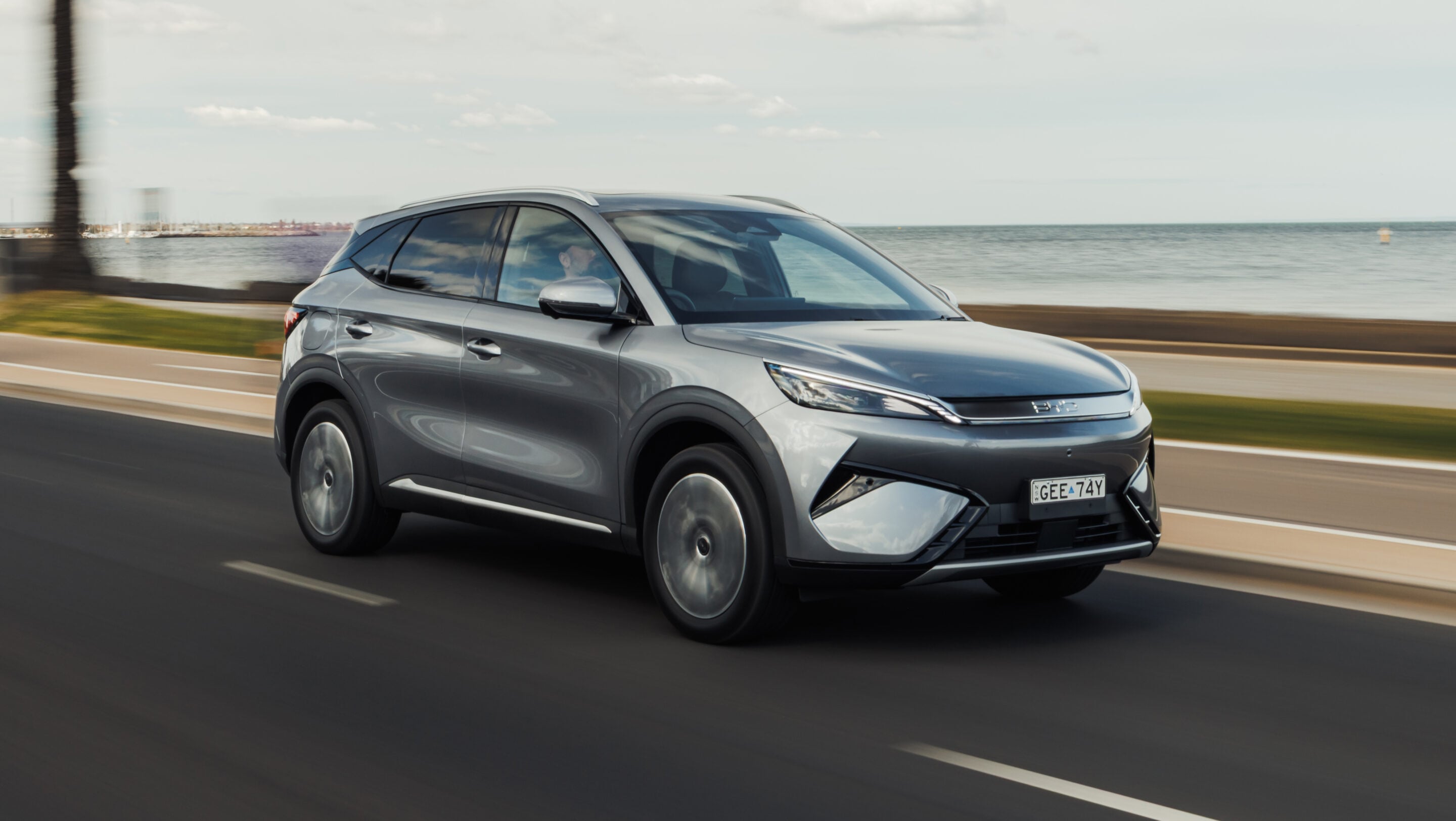Silver SUV driving along a coastal highway with the sea and sky in the background, motion blur suggesting speed.