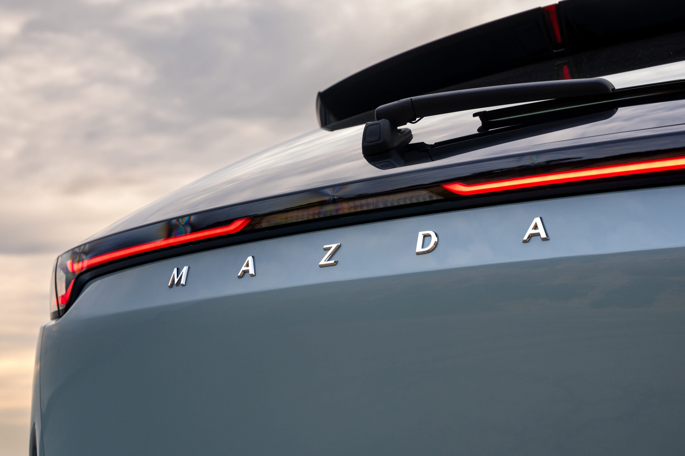 Close-up of the car's rear with 'MAZDA' lettering and a roof-mounted rear wiper, red tail light strip visible on the trunk edge