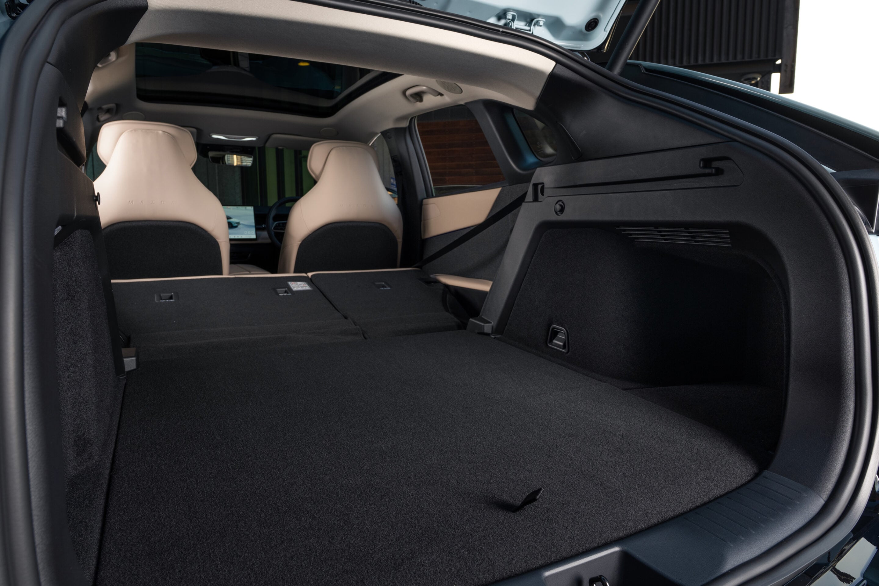 Open SUV trunk with rear seats folded flat, showcasing a large cargo area and beige front seats ahead in a dark-car interior.