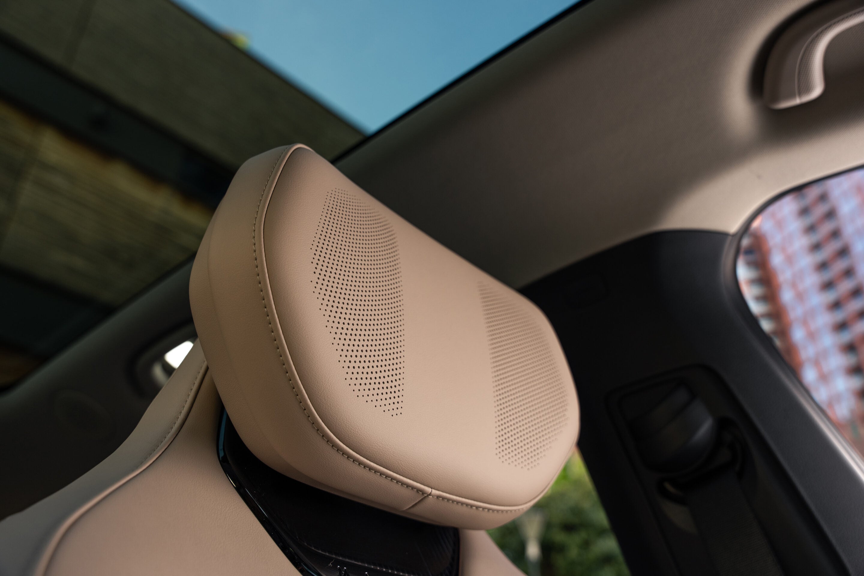 Beige leather car seat headrest with perforated pattern inside a modern vehicle, view of window outside.