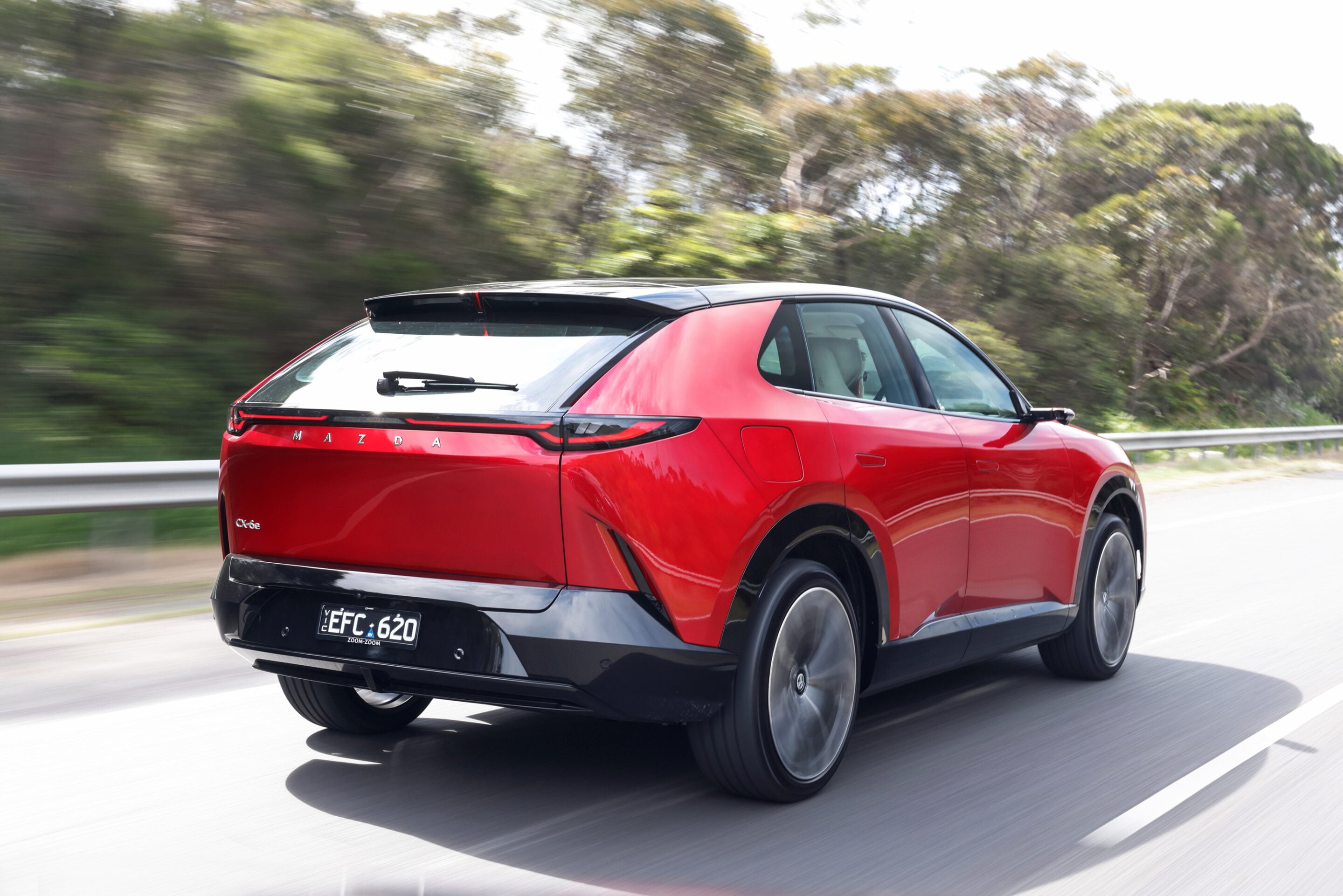 Moving shot of a red Mazda SUV driving on a highway with blurred greenery in the background.