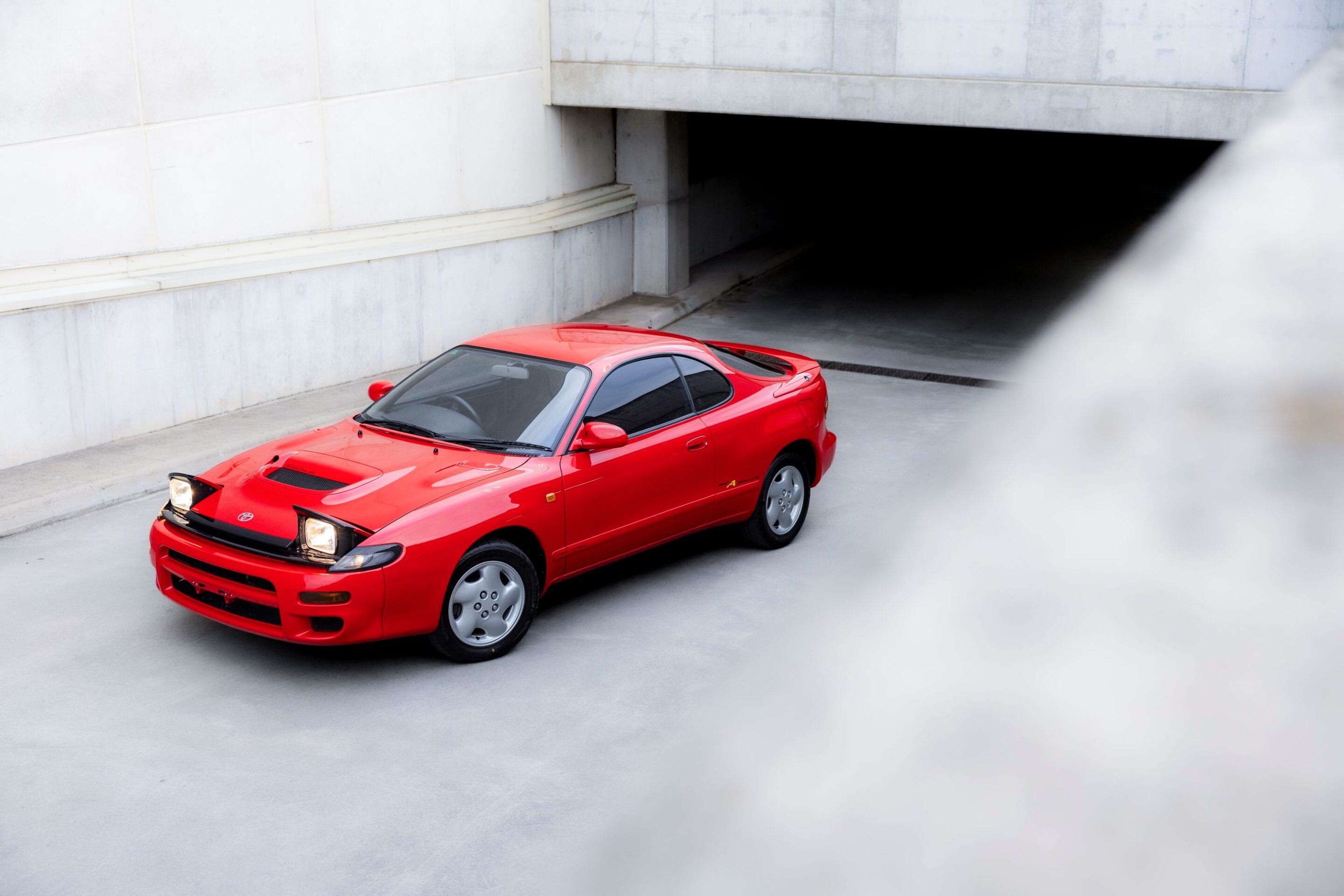 Red sports car on a concrete ramp near a dark garage opening, exiting toward brighter light.