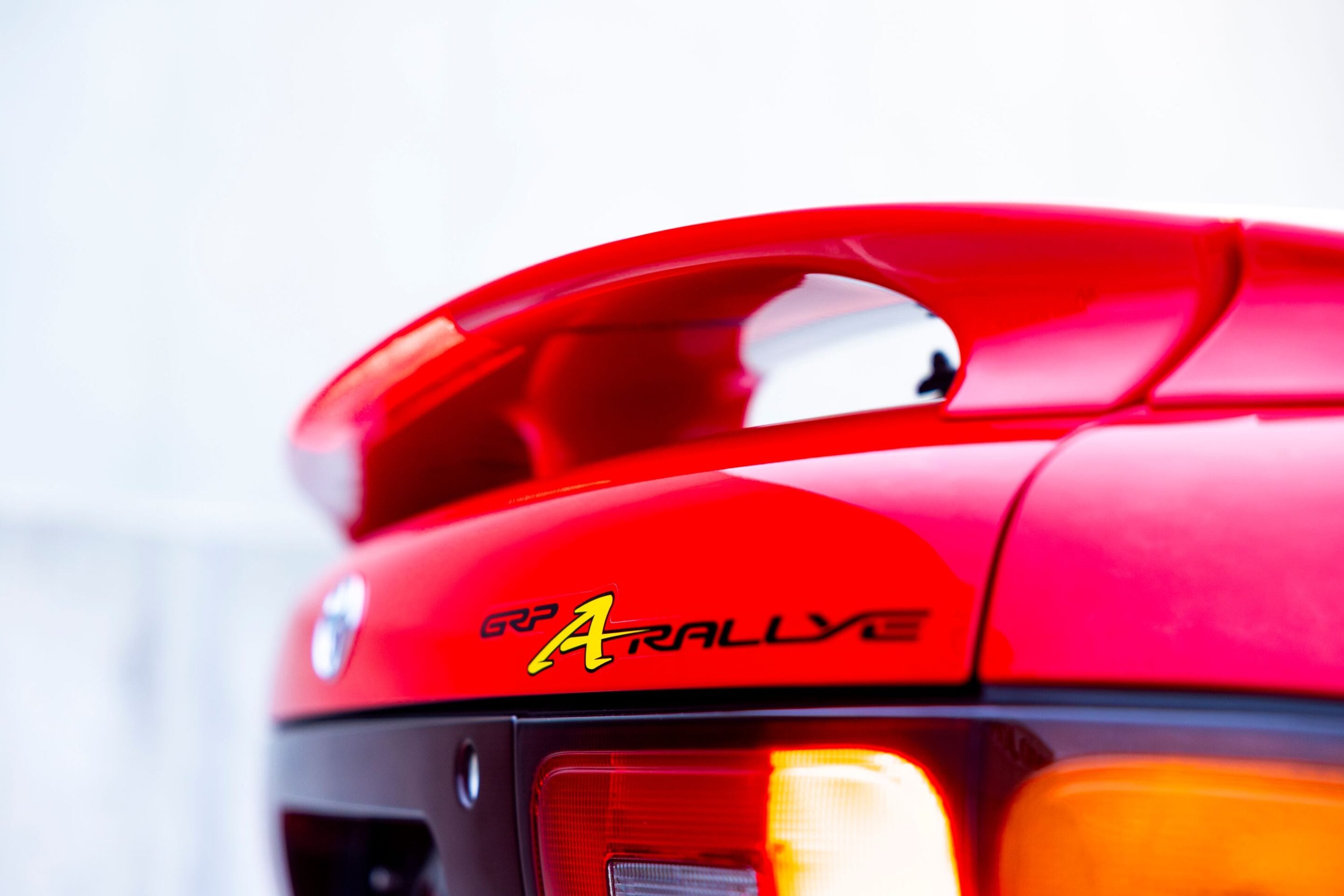 Close-up of a bright red car’s rear, showing the tail light and curving body panel.