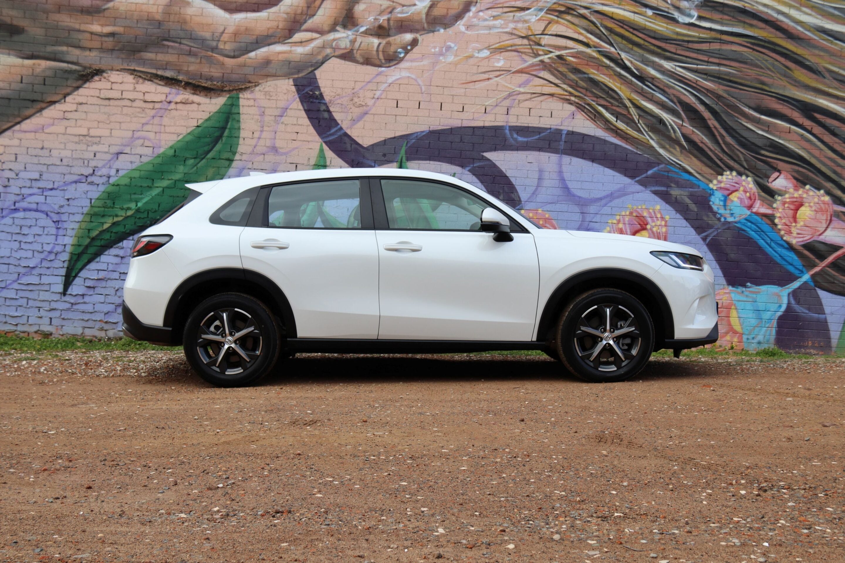 White midsize SUV parked in front of a bright graffiti mural on a brick wall behind it.