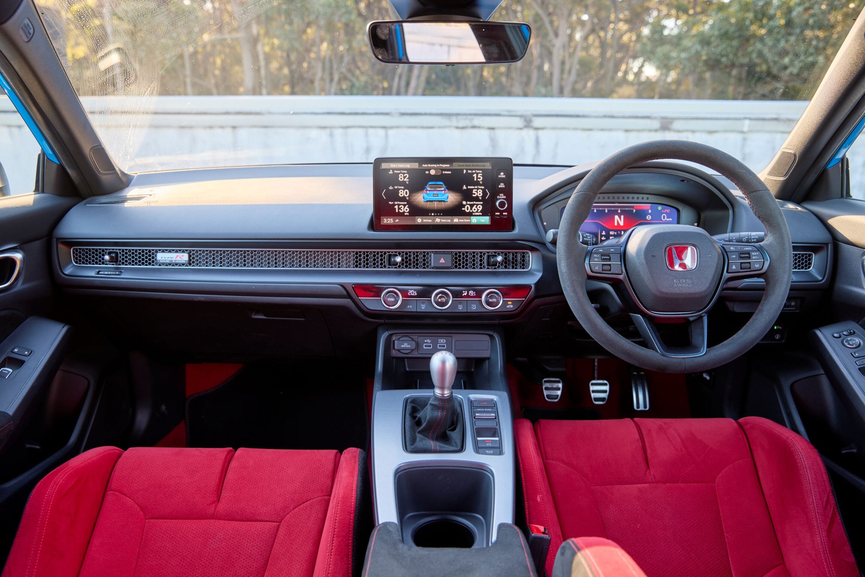 Front interior of a car with bright red seats, a central touchscreen display, and a steering wheel visible on the right side of the image.
