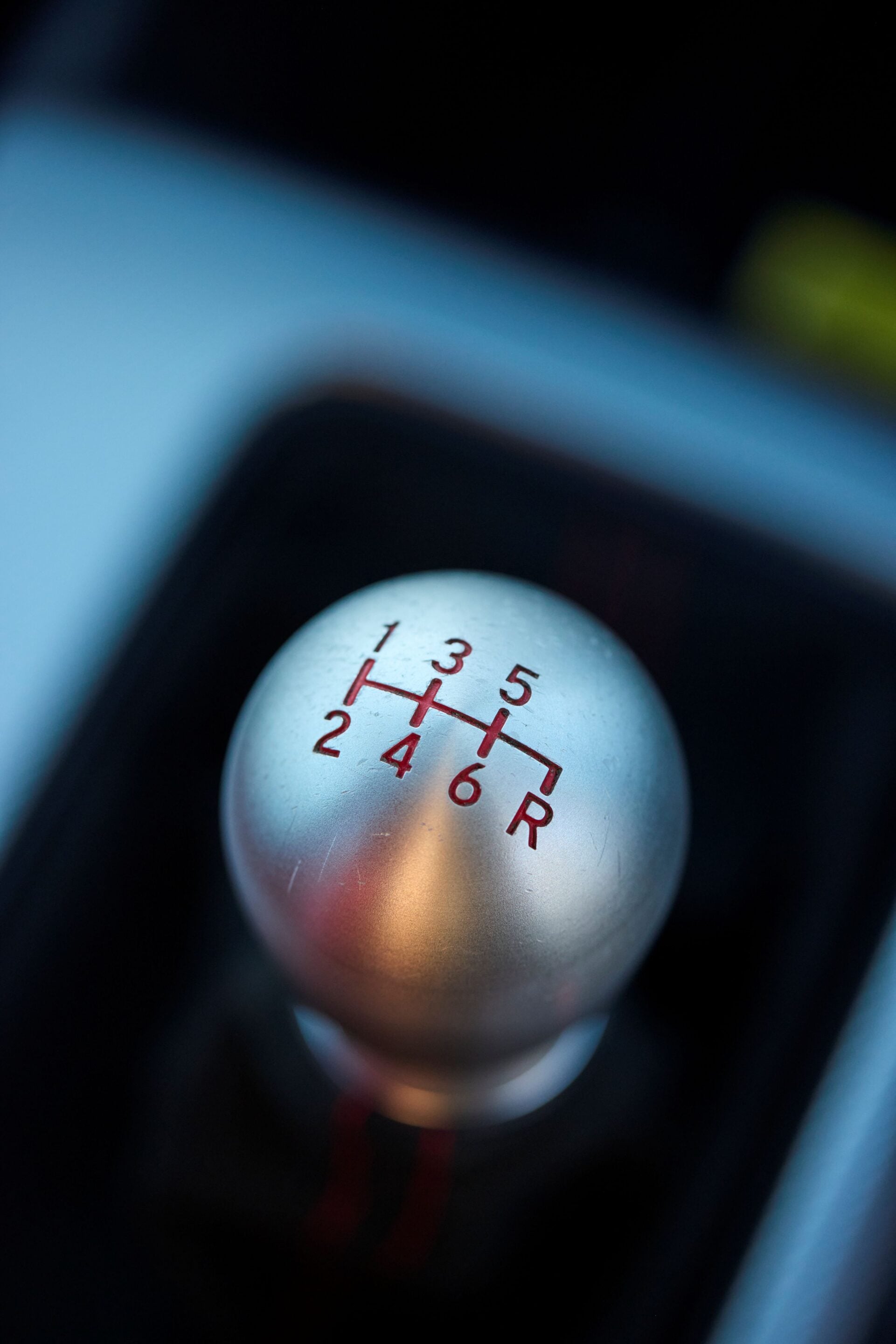Close-up of a car manual gear shift knob with red shift pattern on a silver surface in a dark interior.