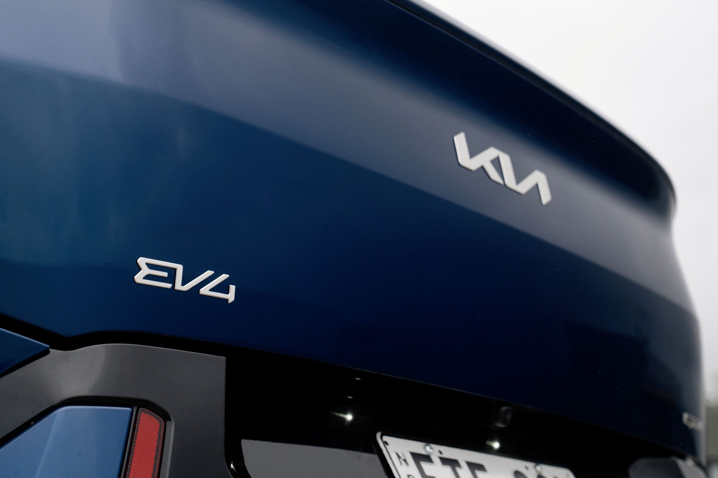 Close-up of a dark blue car rear with a silver 'EV4' badge visible on the trunk area.