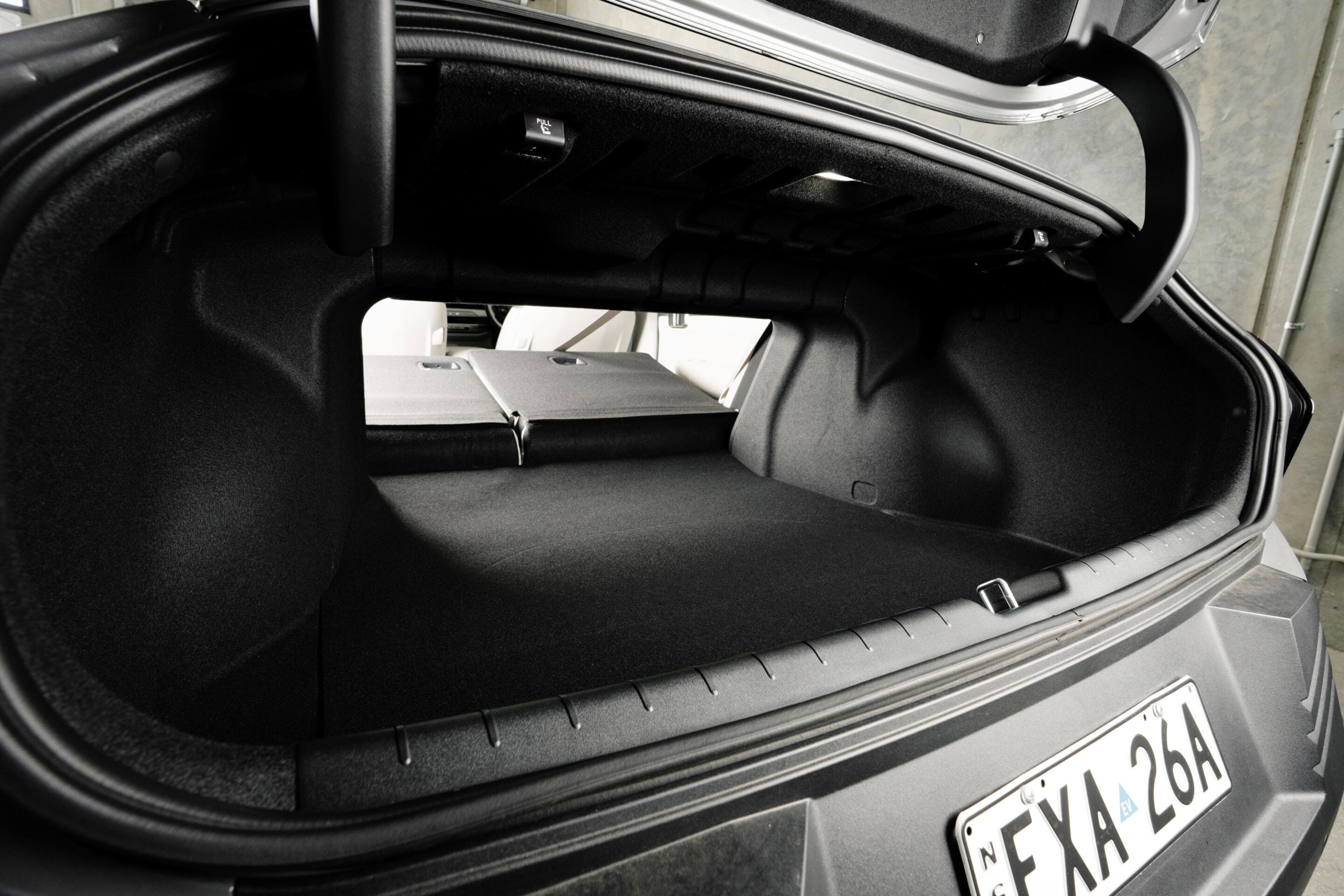 Open car trunk in a dark SUV, showing black carpeted cargo area with rear seats folded and a visible license plate on the bumper.