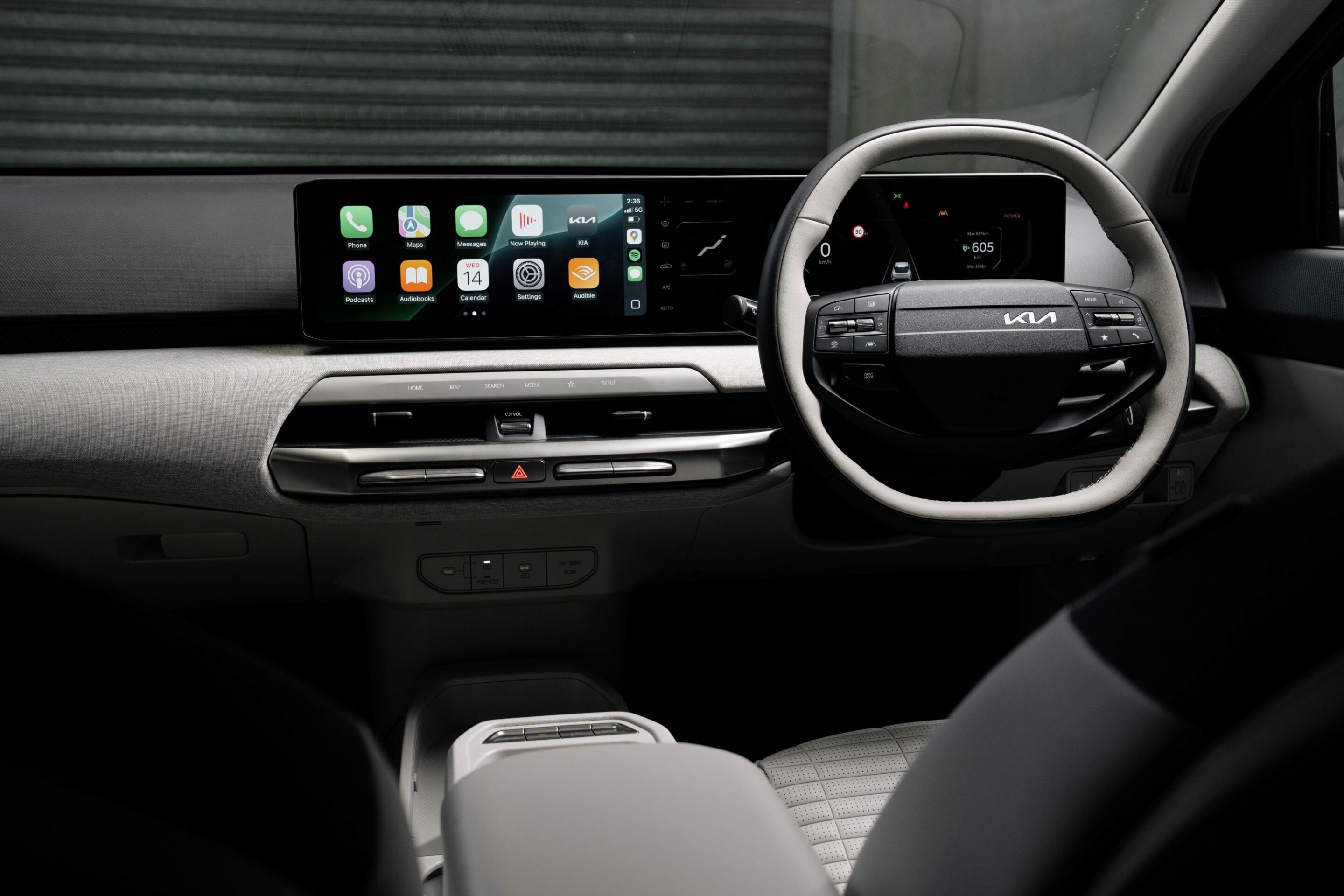 Interior of a car showing a wide horizontal touchscreen dashboard with app icons and a right-side steering wheel in the foreground on a dark interior.