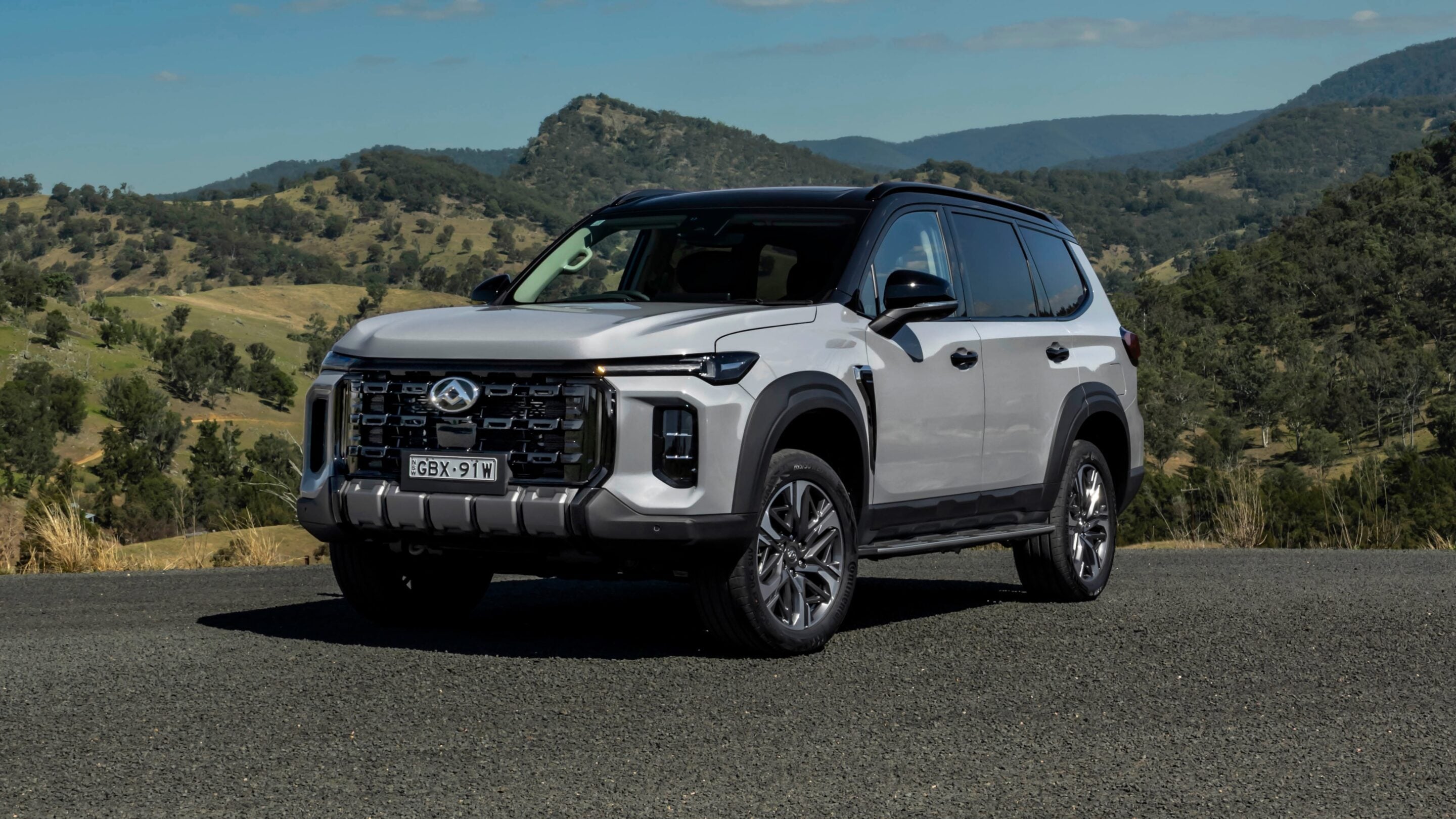 Silver SUV parked on a scenic hillside road with rolling green hills in the background.
