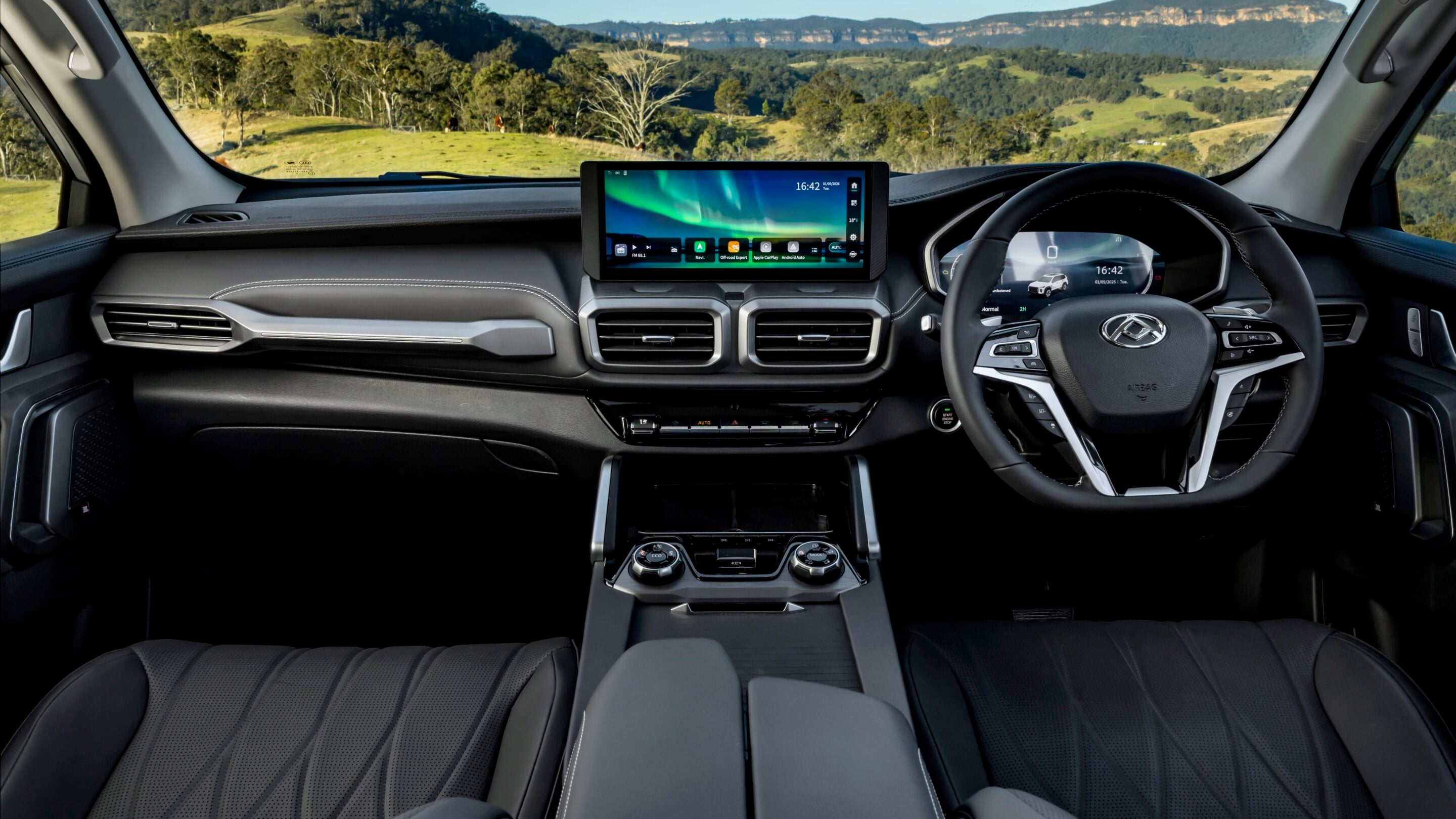 Interior of a modern car cabin with a large central touchscreen and steering wheel, countryside visible through the windshield