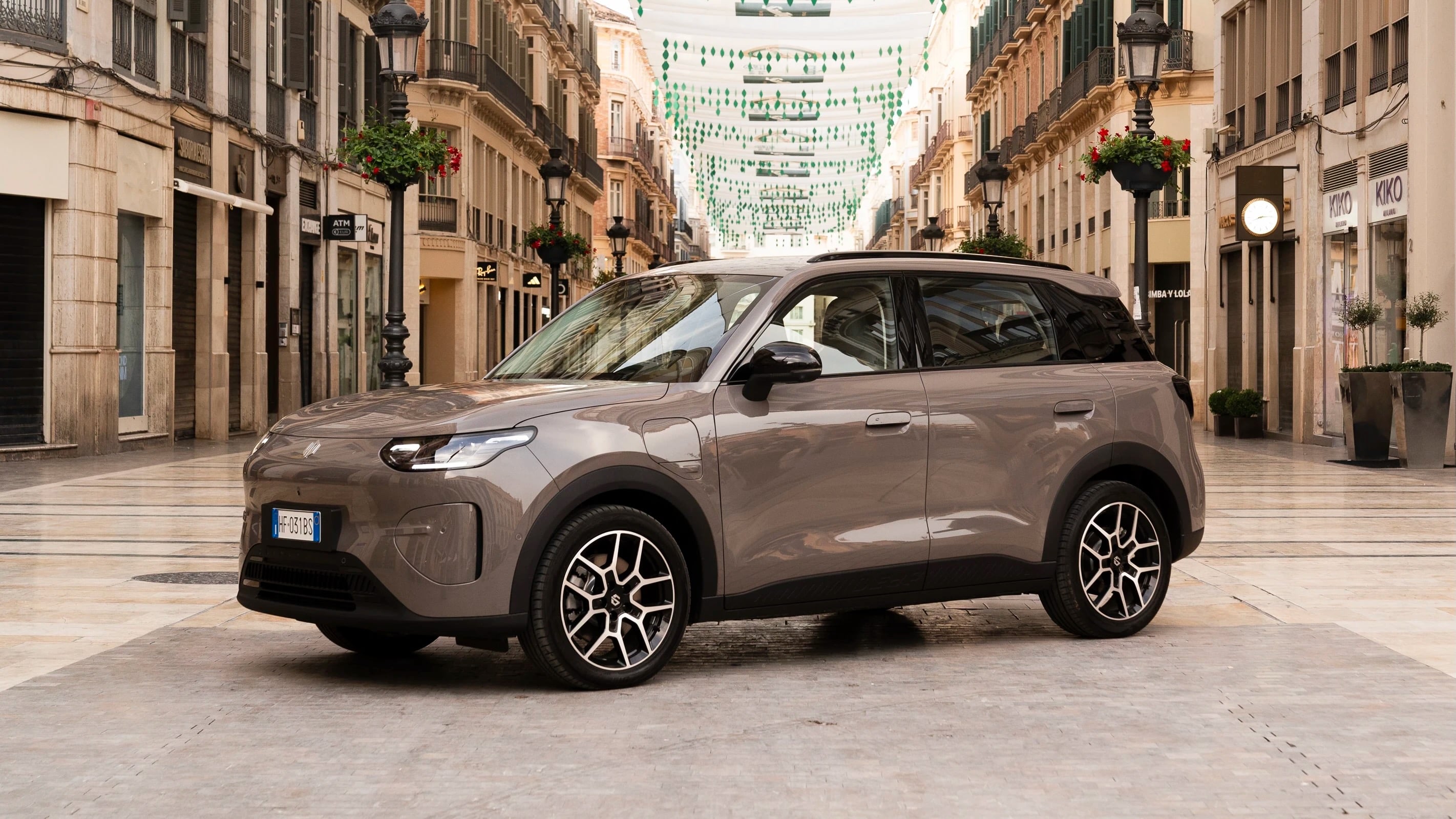 Gray SUV parked on a pedestrian street lined with shops and hanging green decorations