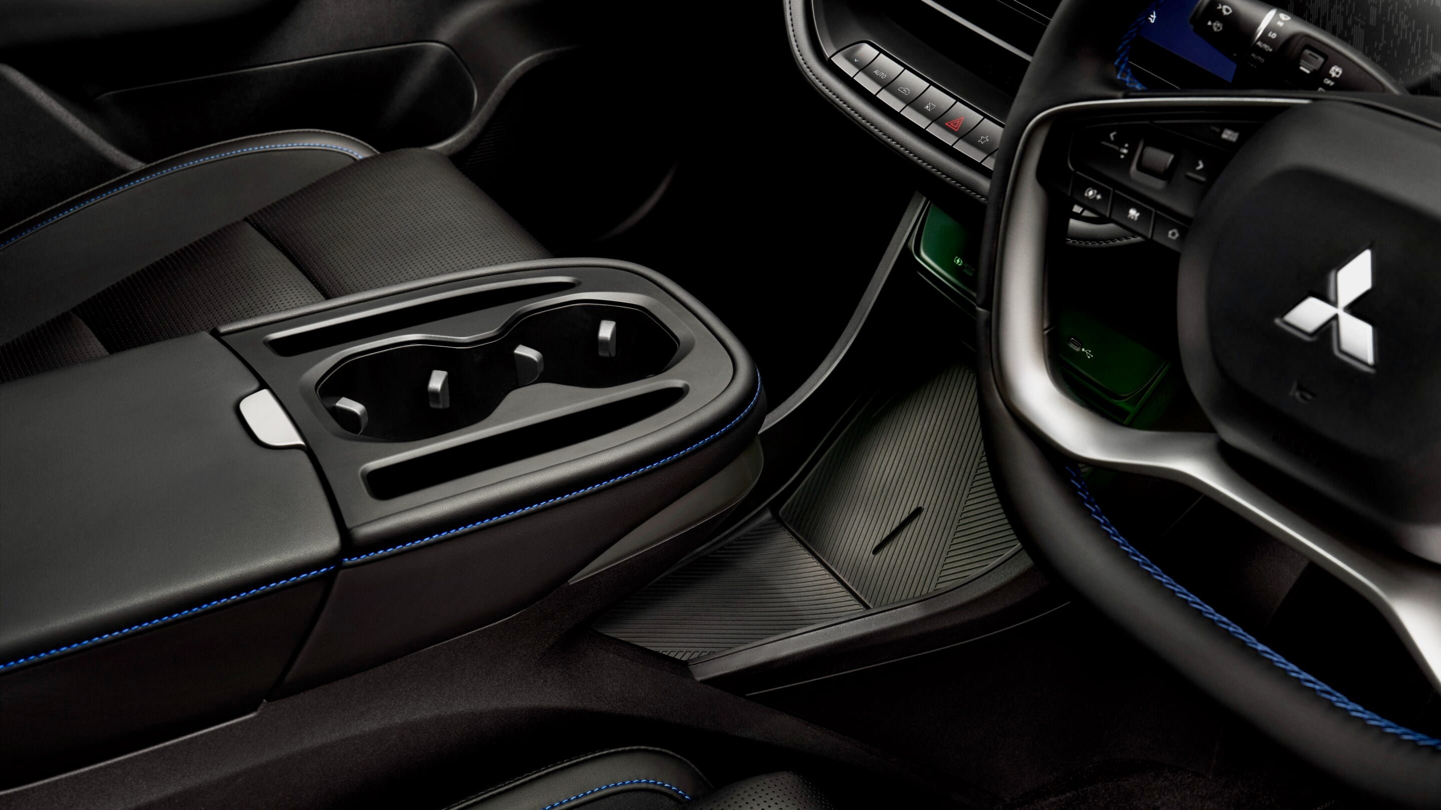 Close-up of a black car interior showing the center console, cupholders, and blue-stitched seats beside a steering wheel with a Mitsubishi logo in the foreground