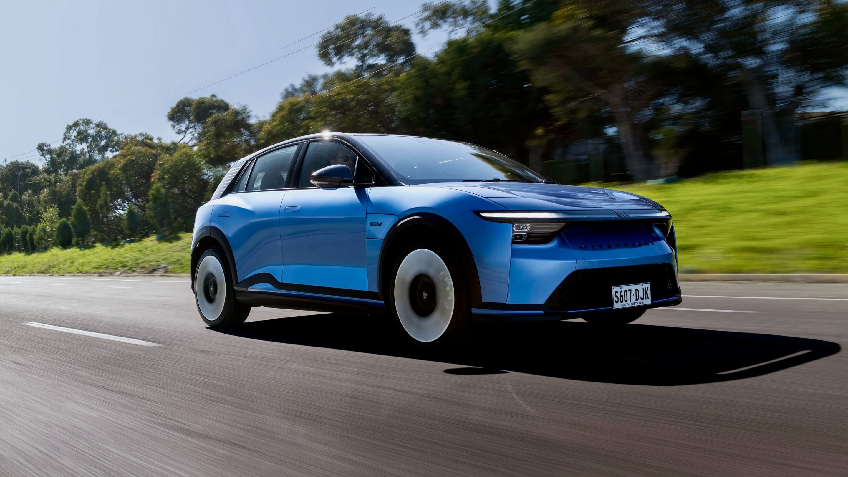 Blue electric SUV speeding along a highway with trees in the background and SA license plate S607-DJK; motion blur on the road ahead.