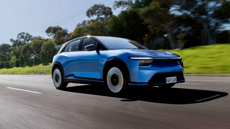 Blue electric SUV speeding along a highway with trees in the background and SA license plate S607-DJK; motion blur on the road ahead.
