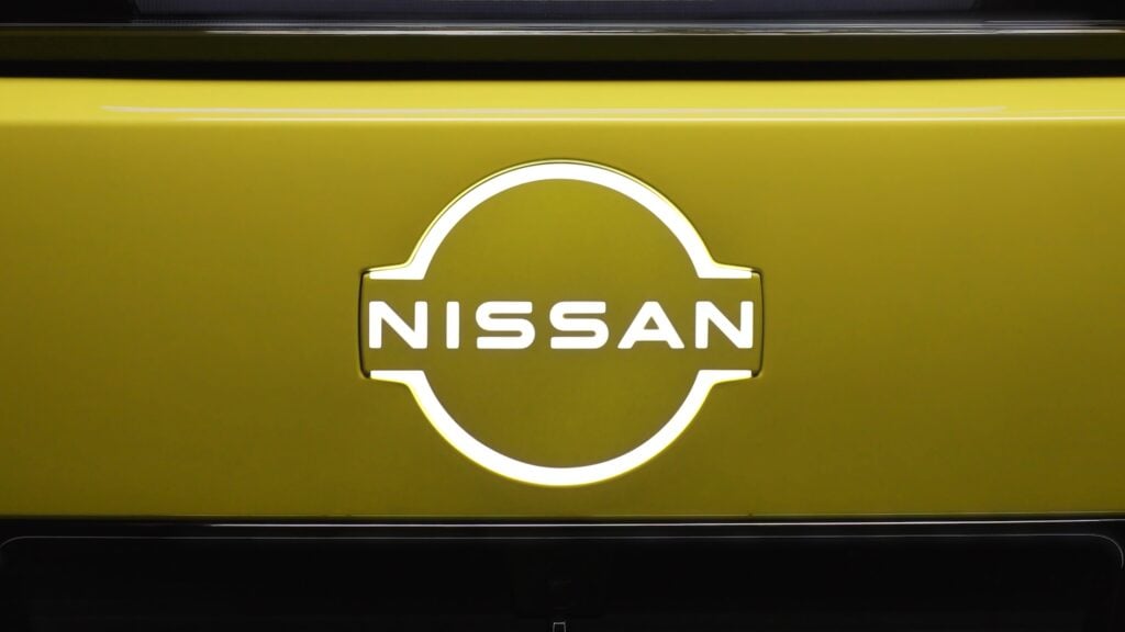 Close-up of the Nissan circular logo on a yellow car surface, with the word NISSAN centered inside the emblem.