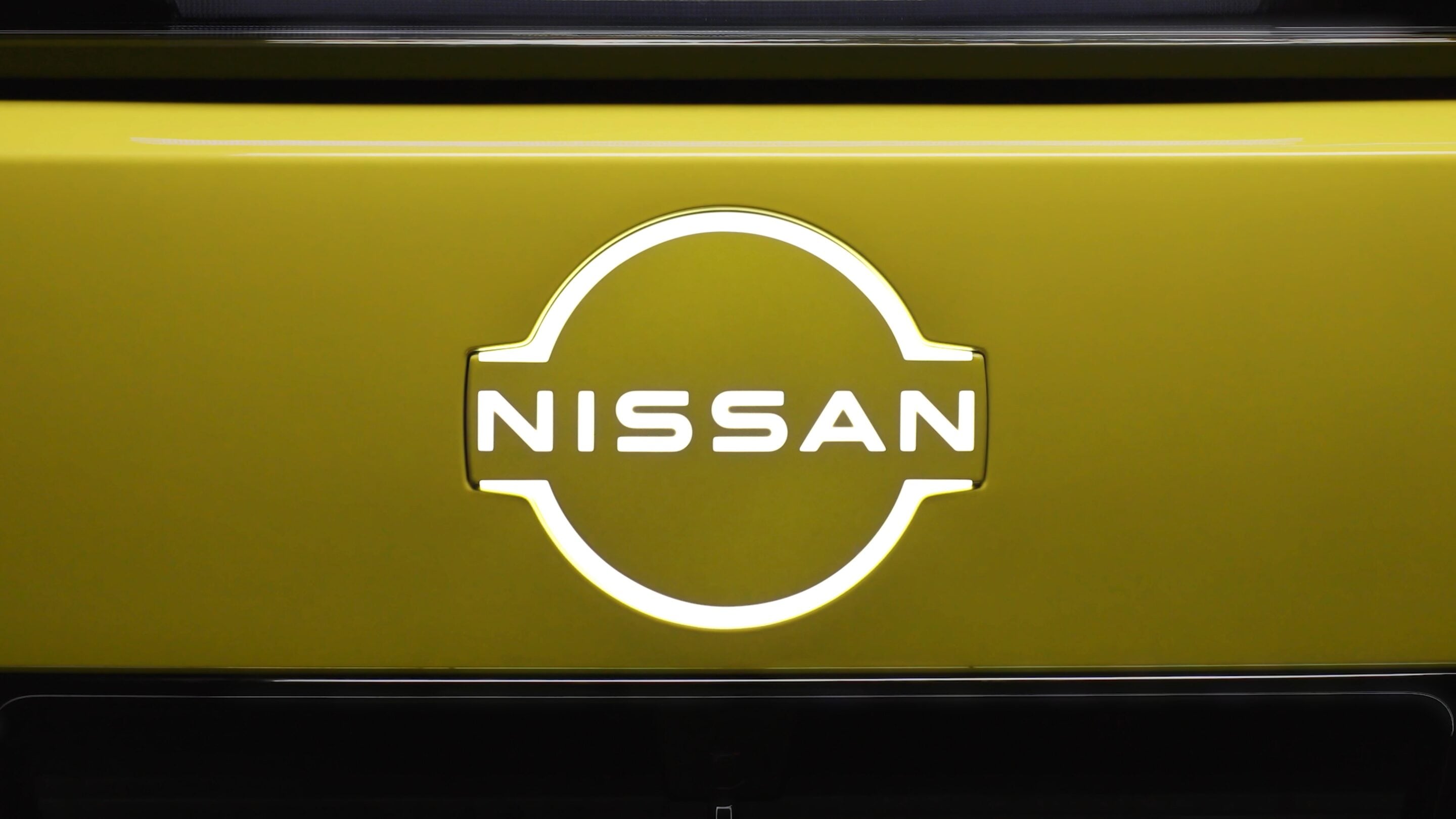 Close-up of the Nissan circular logo on a yellow car surface, with the word NISSAN centered inside the emblem.