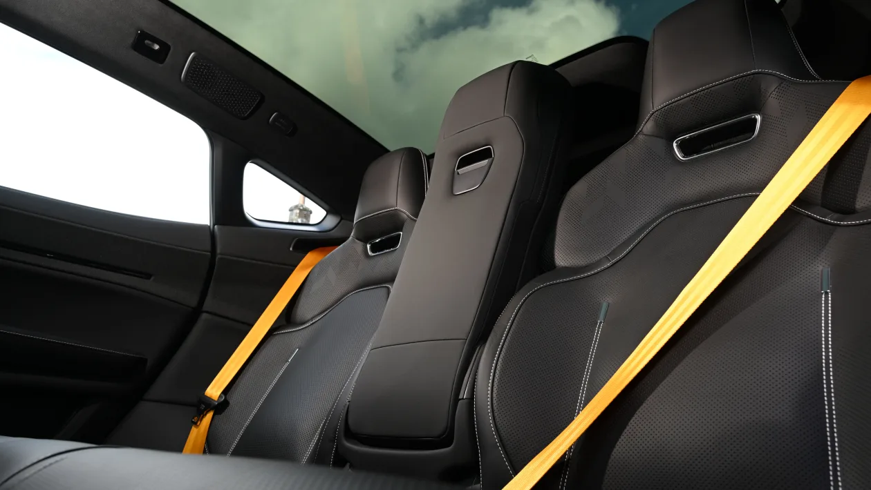Back seats of a luxury car with black leather upholstery and bright yellow seat belts.
