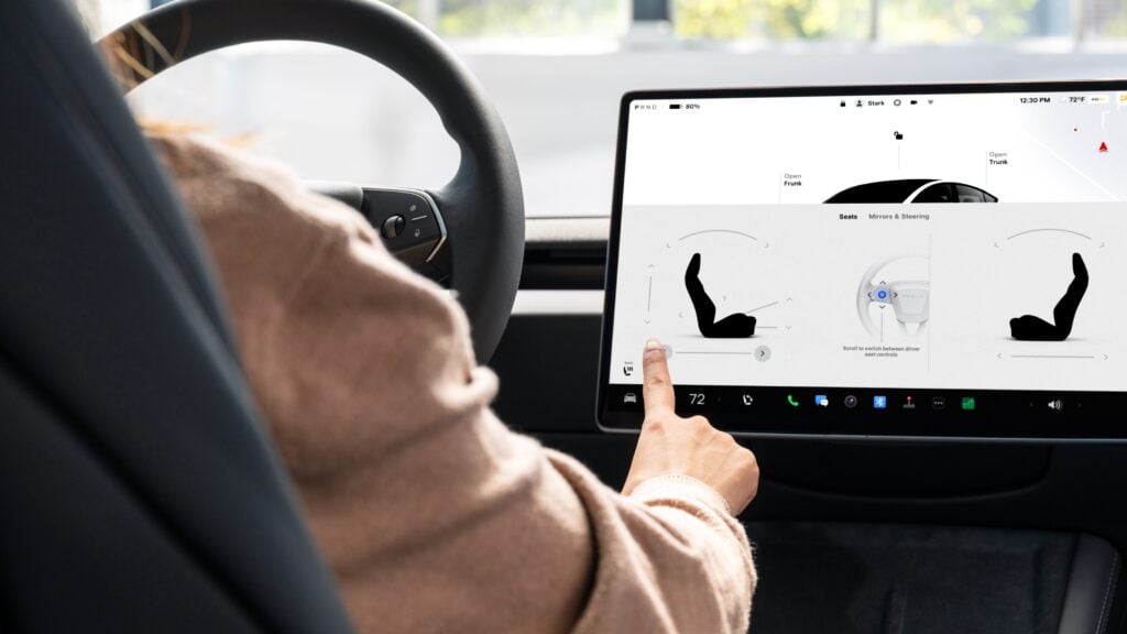 Driver in a car uses a large touchscreen to adjust seat and steering controls.