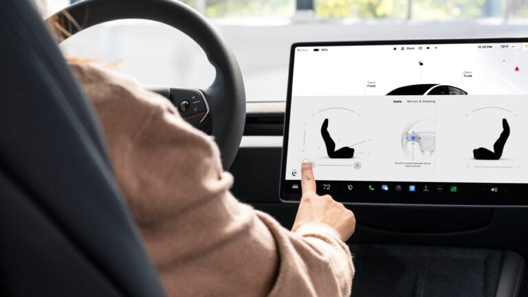 Driver in a car uses a large touchscreen to adjust seat and steering controls.