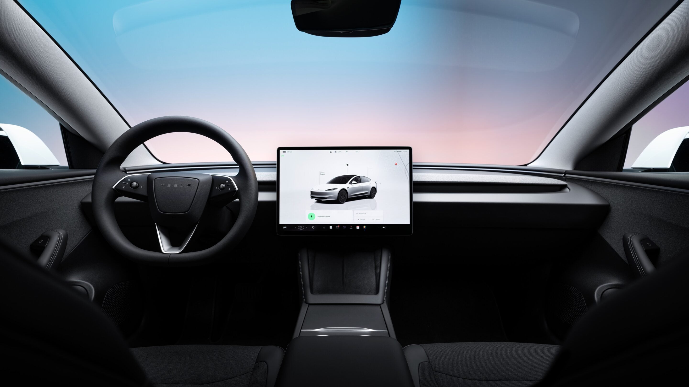 Tesla interior: steering wheel and large central touchscreen showing a white car on the display, dark dashboard and panoramic windshield view.