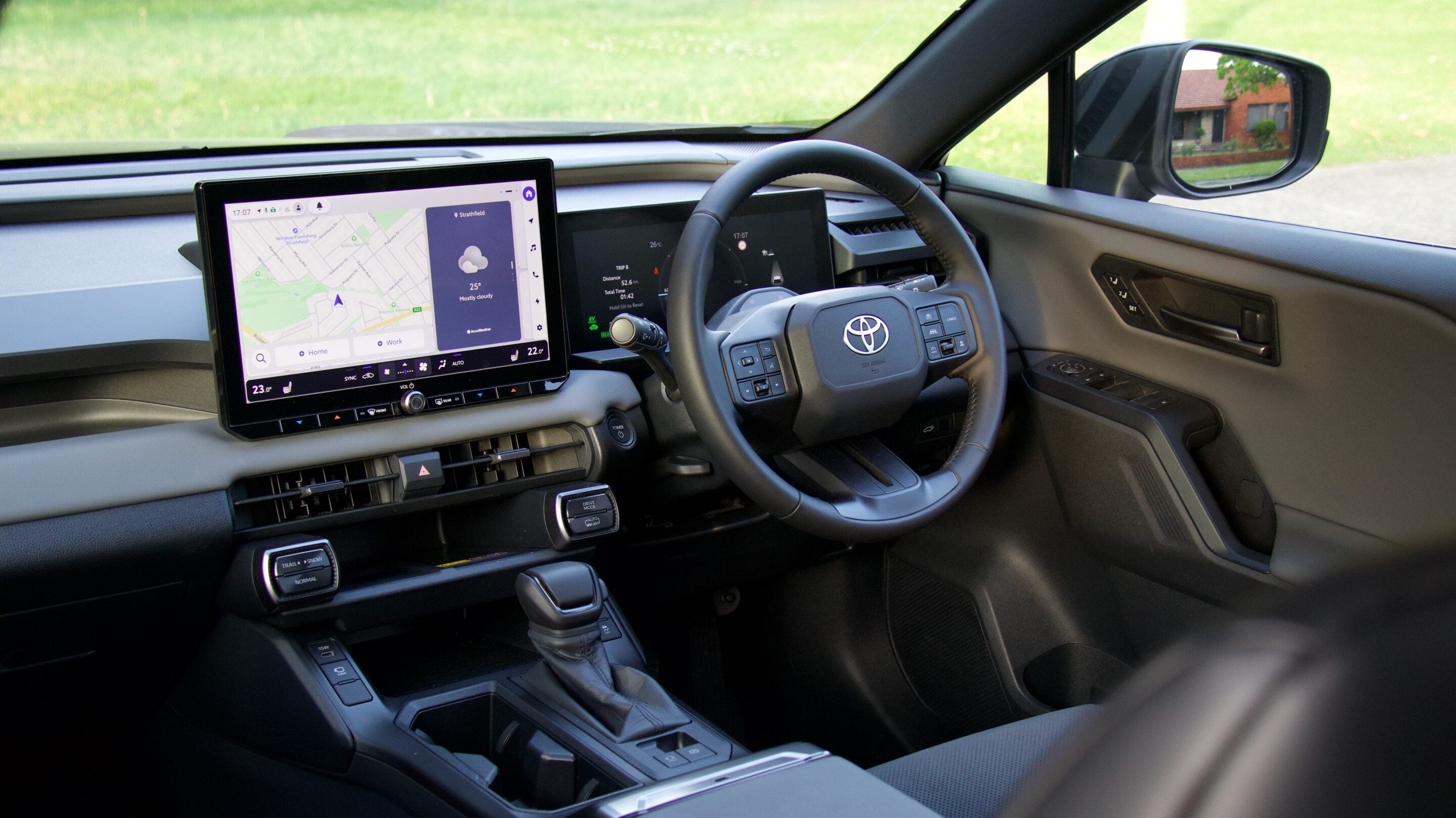 Modern car interior focusing on a large center touchscreen displaying a navigation map and climate info, with a steering wheel and instrument cluster nearby.