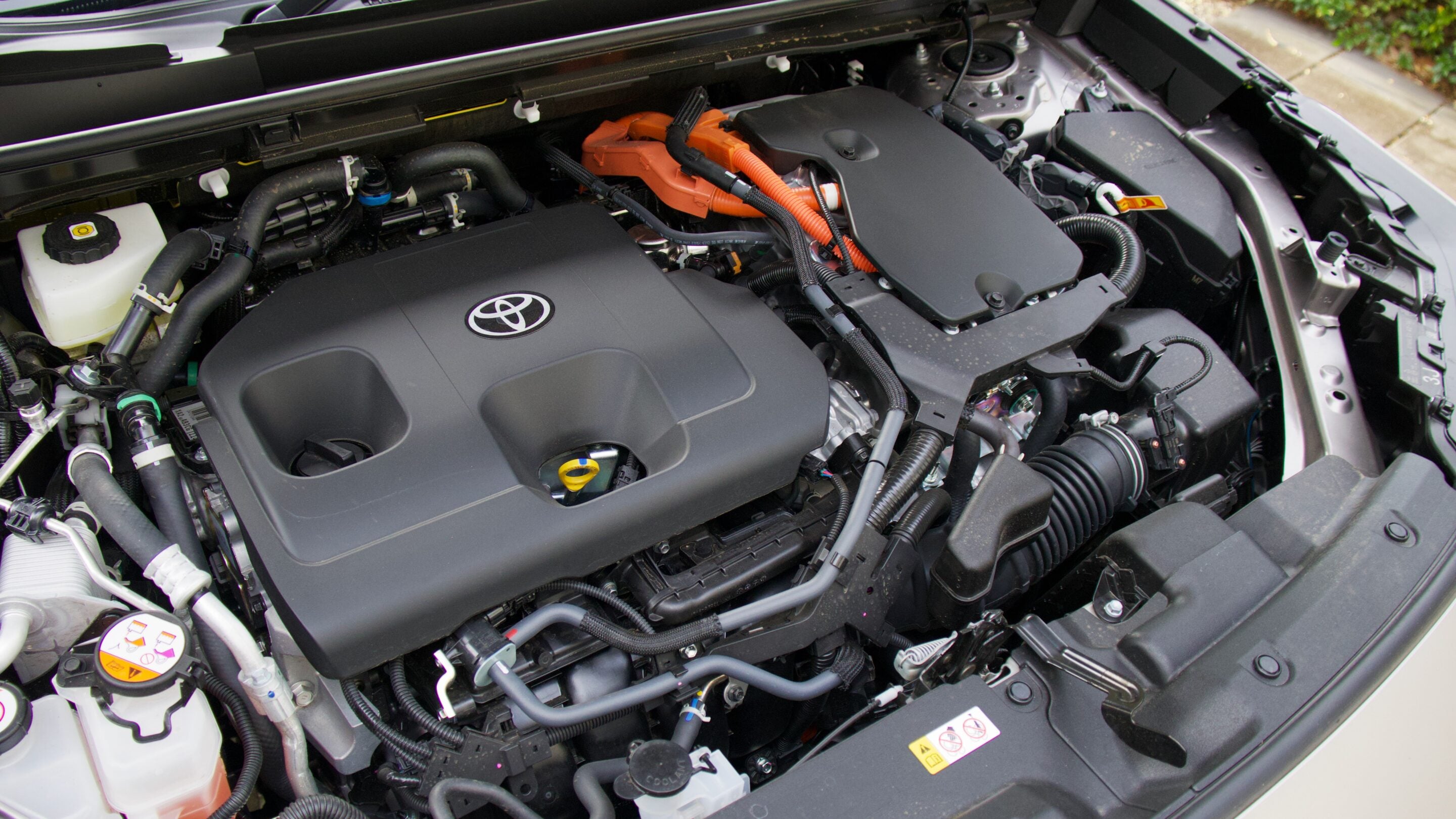 Front view of a Toyota engine bay with a large plastic engine cover bearing the Toyota emblem and various hoses and cables behind it