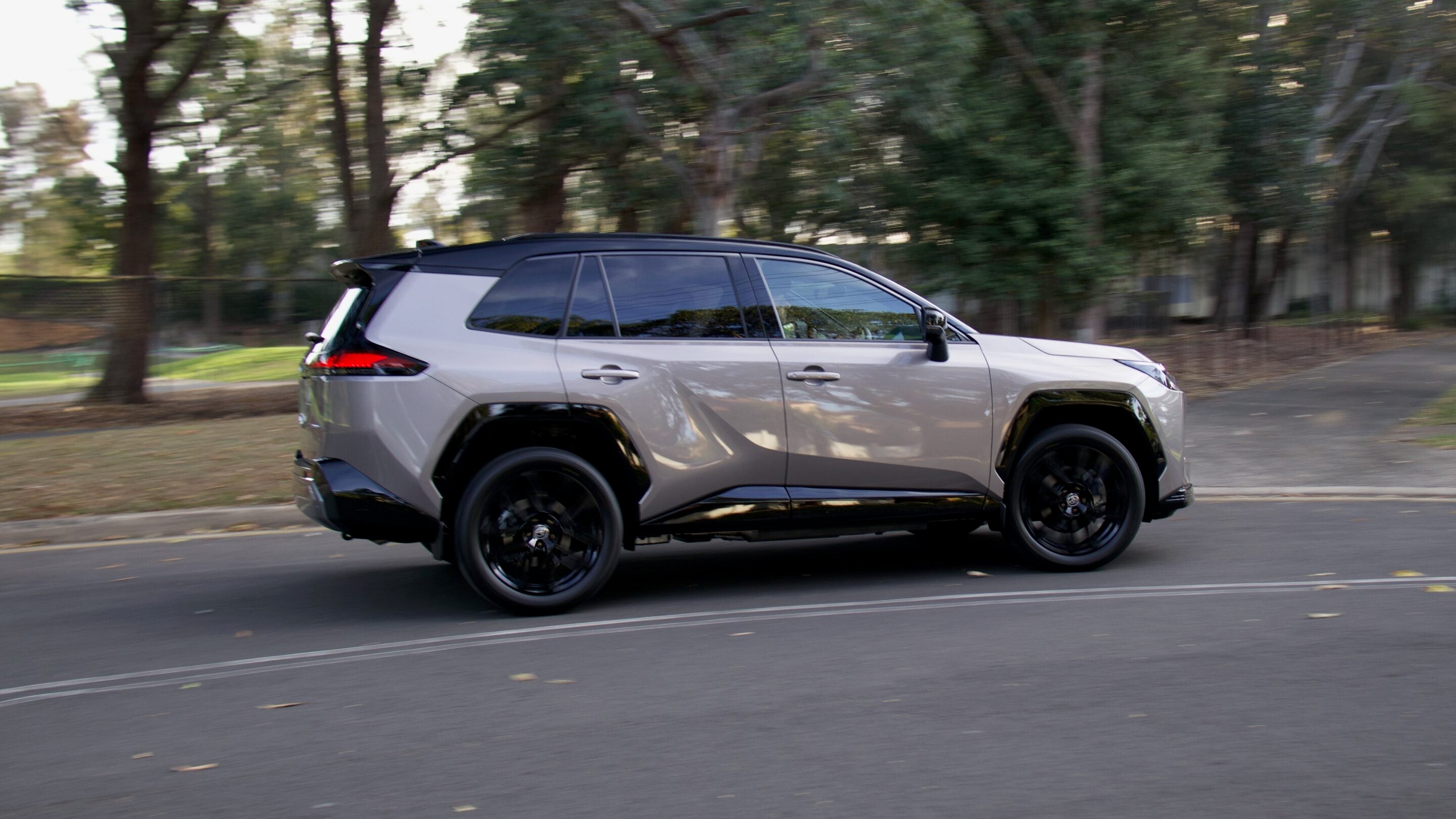 Side view of a silver SUV driving on a tree-lined street, motion blur indicating speed.