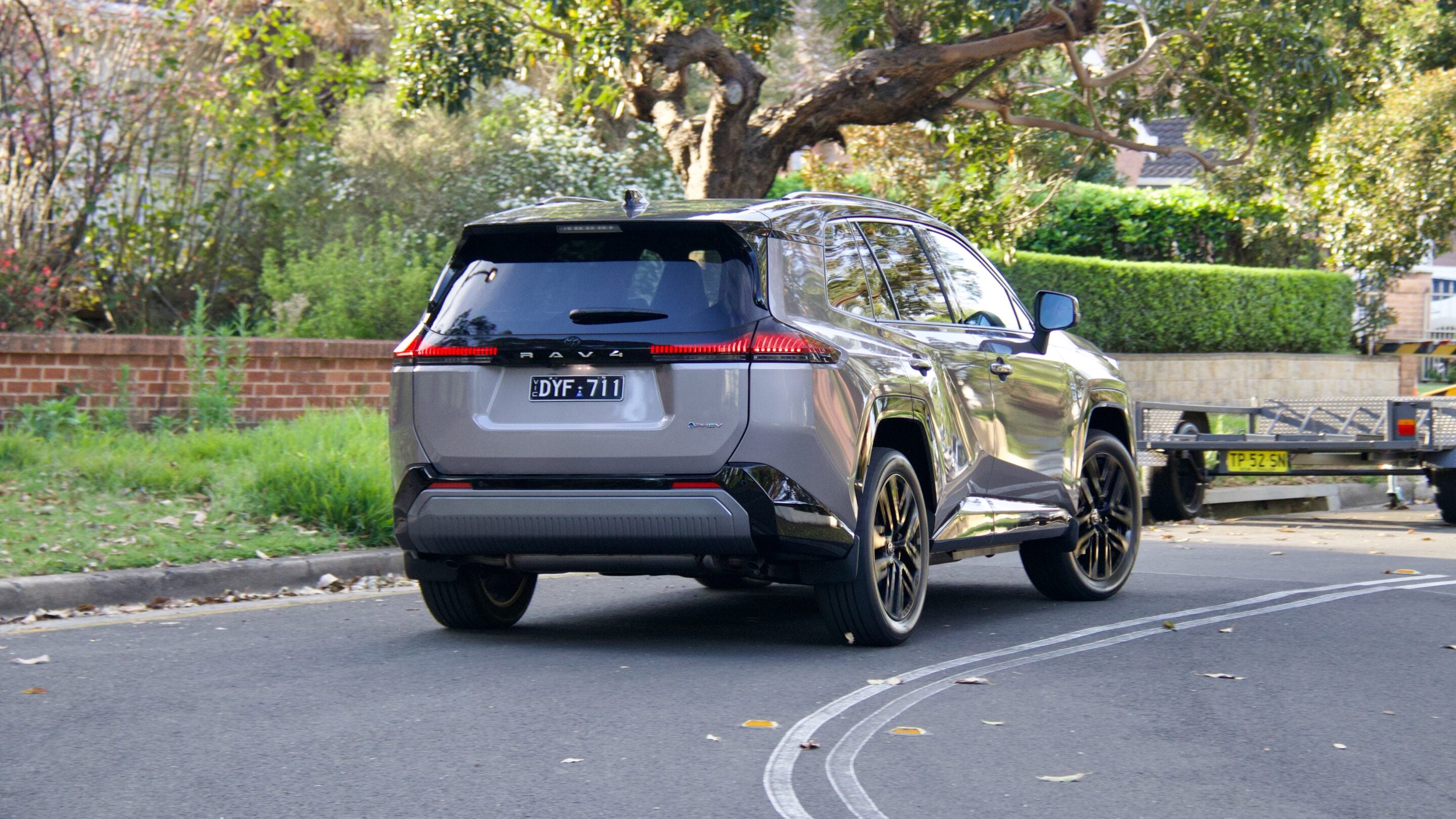 Rear three-quarter view of a silver SUV (RAV4) with a trailer attached on a suburban street.