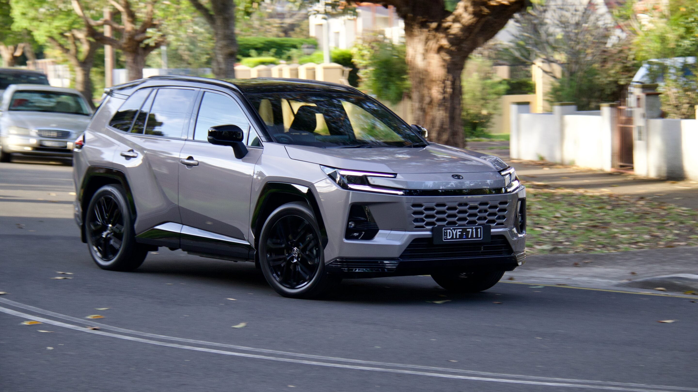 Silver SUV in motion on a suburban street, front angled view with blurred green trees in the background, license plate DYF 711 visible