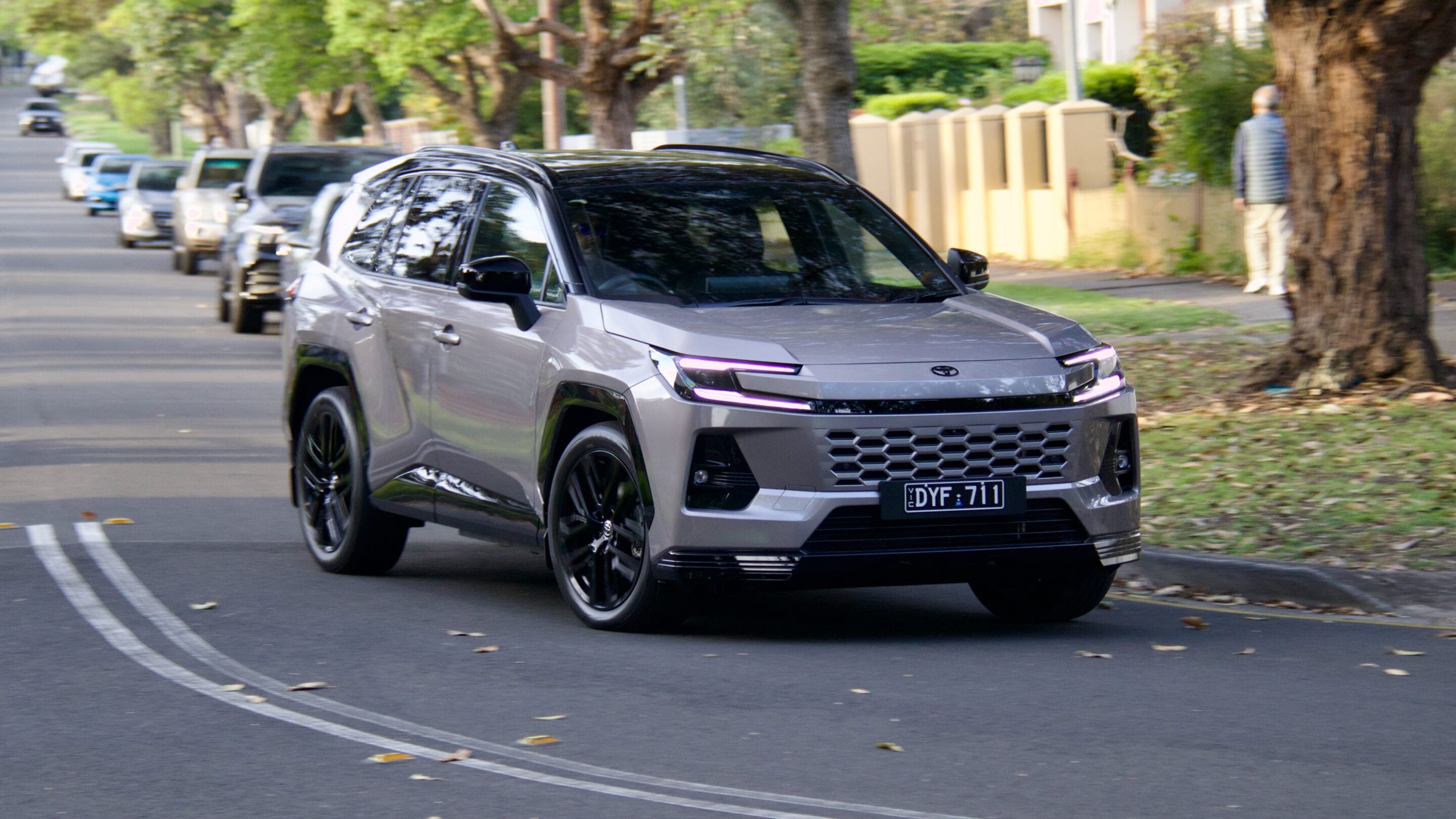 Silver SUV driving down a suburban street, leaves on the road, front view with license plate DYF 711 visible in the foreground.