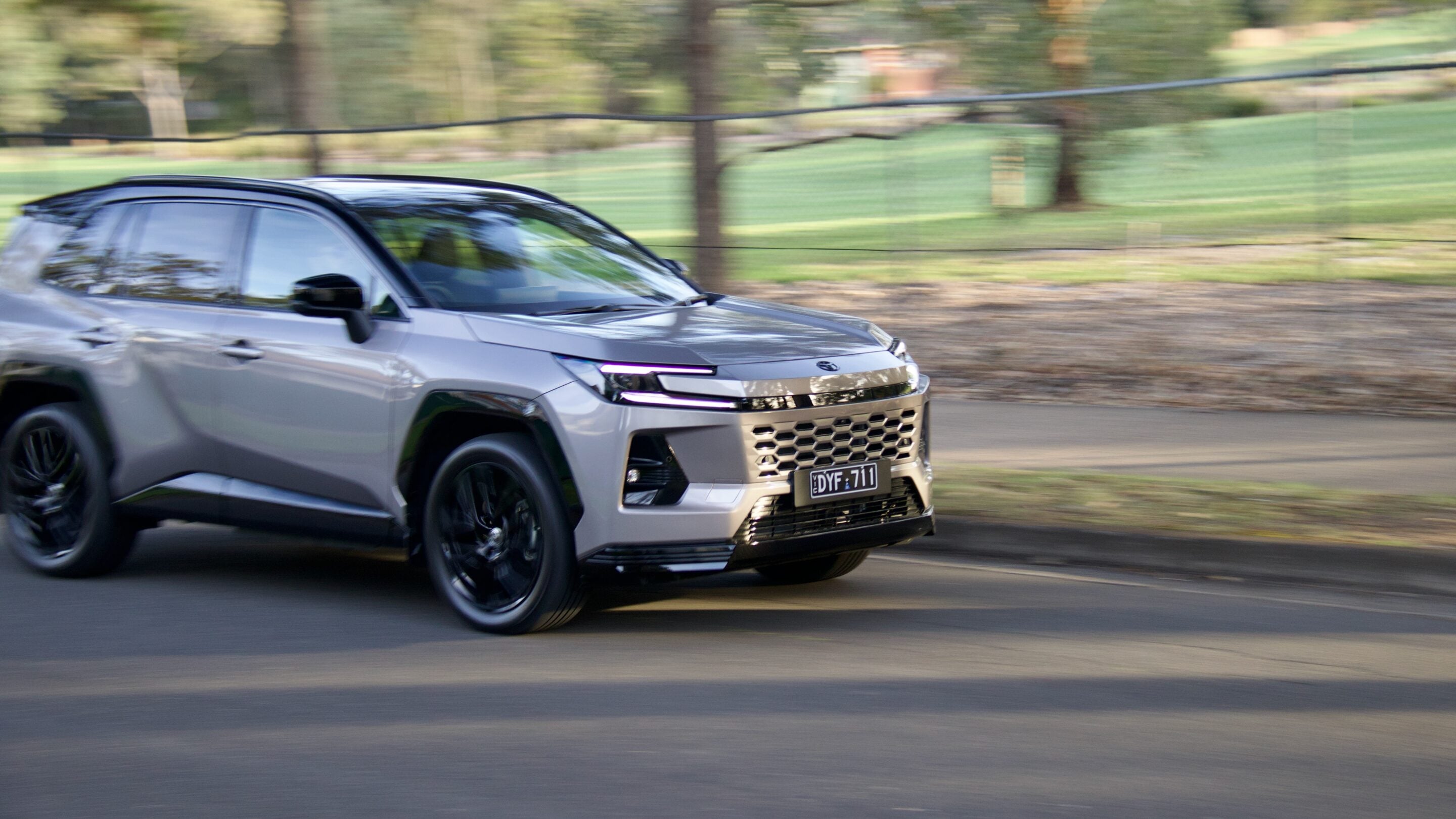 Silver SUV driving on a road with blurred green trees in the background, indicating motion blur from speed.