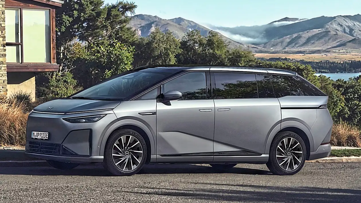 Silver futuristic minivan parked on a road with a mountain landscape in the background
