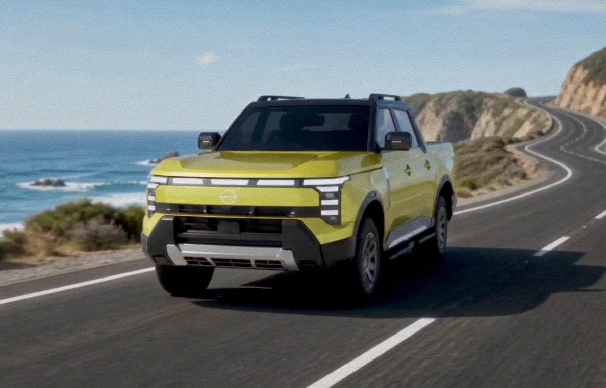 Front three-quarter of a 2027 Nissan Navara Pro PHEV driving on a coastal highway beside ocean cliffs.