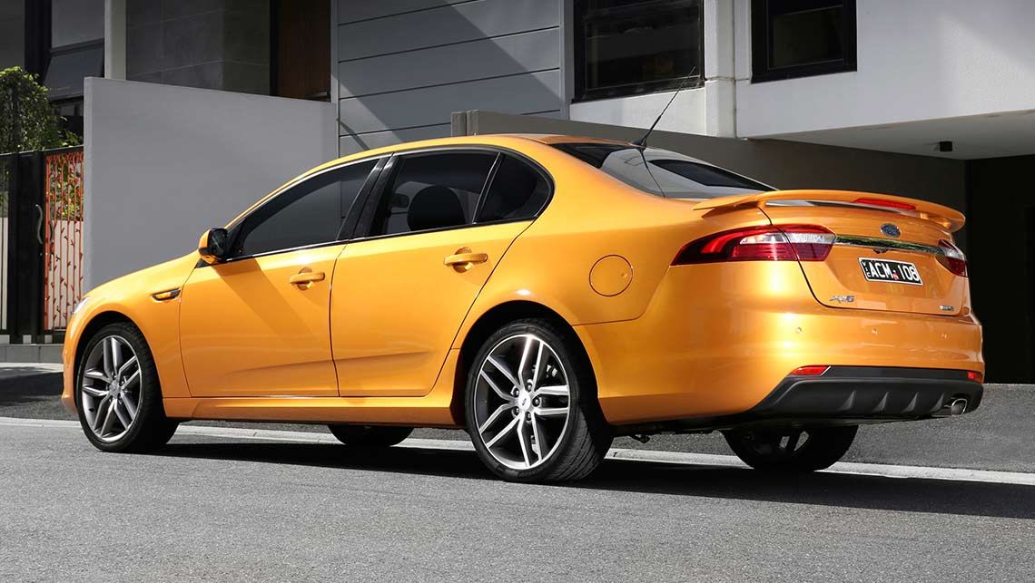 Orange sedan parked on a residential street with a modern house in the background, seen from rear-side angle.